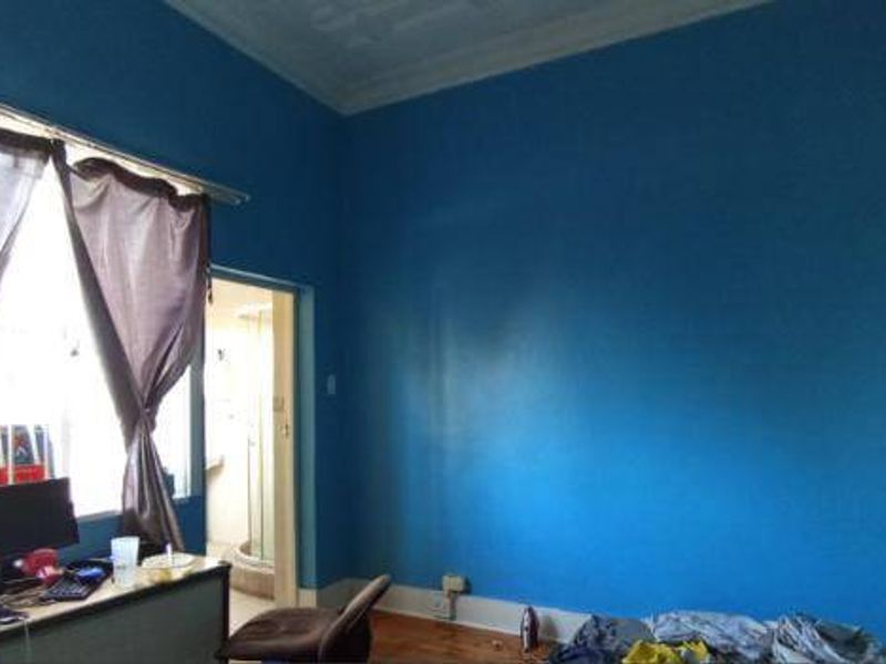 A bedroom featuring timber flooring and ornate ceiling cornicing, currently finished with bold blue wall paint.