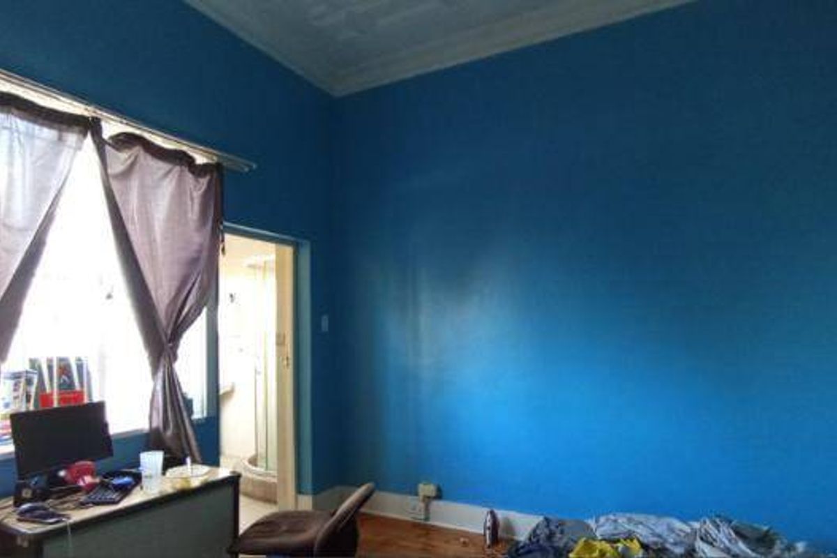 A bedroom featuring timber flooring and ornate ceiling cornicing, currently finished with bold blue wall paint.