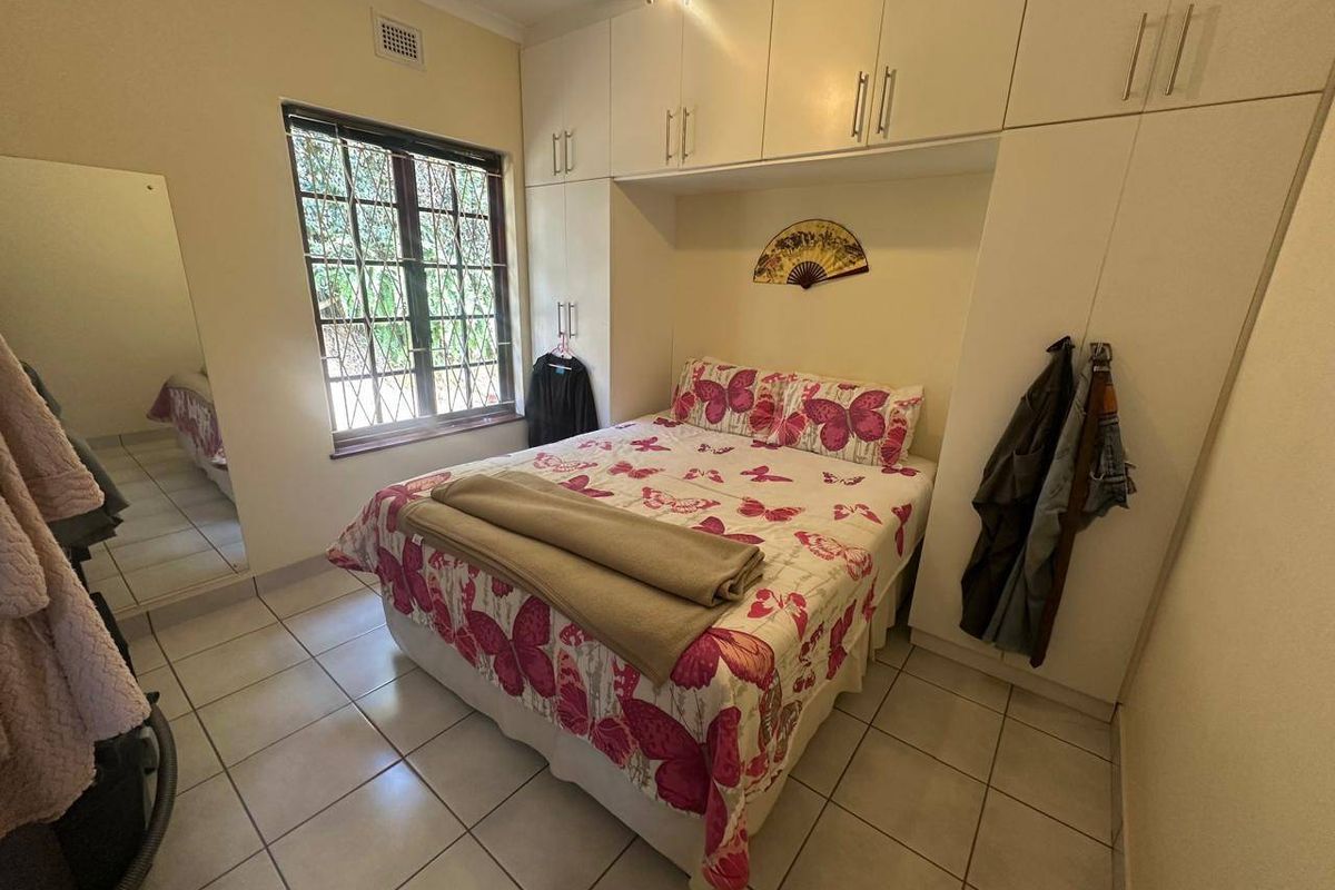 A functional bedroom featuring built-in cupboards, tiled flooring, and a window with security bars.