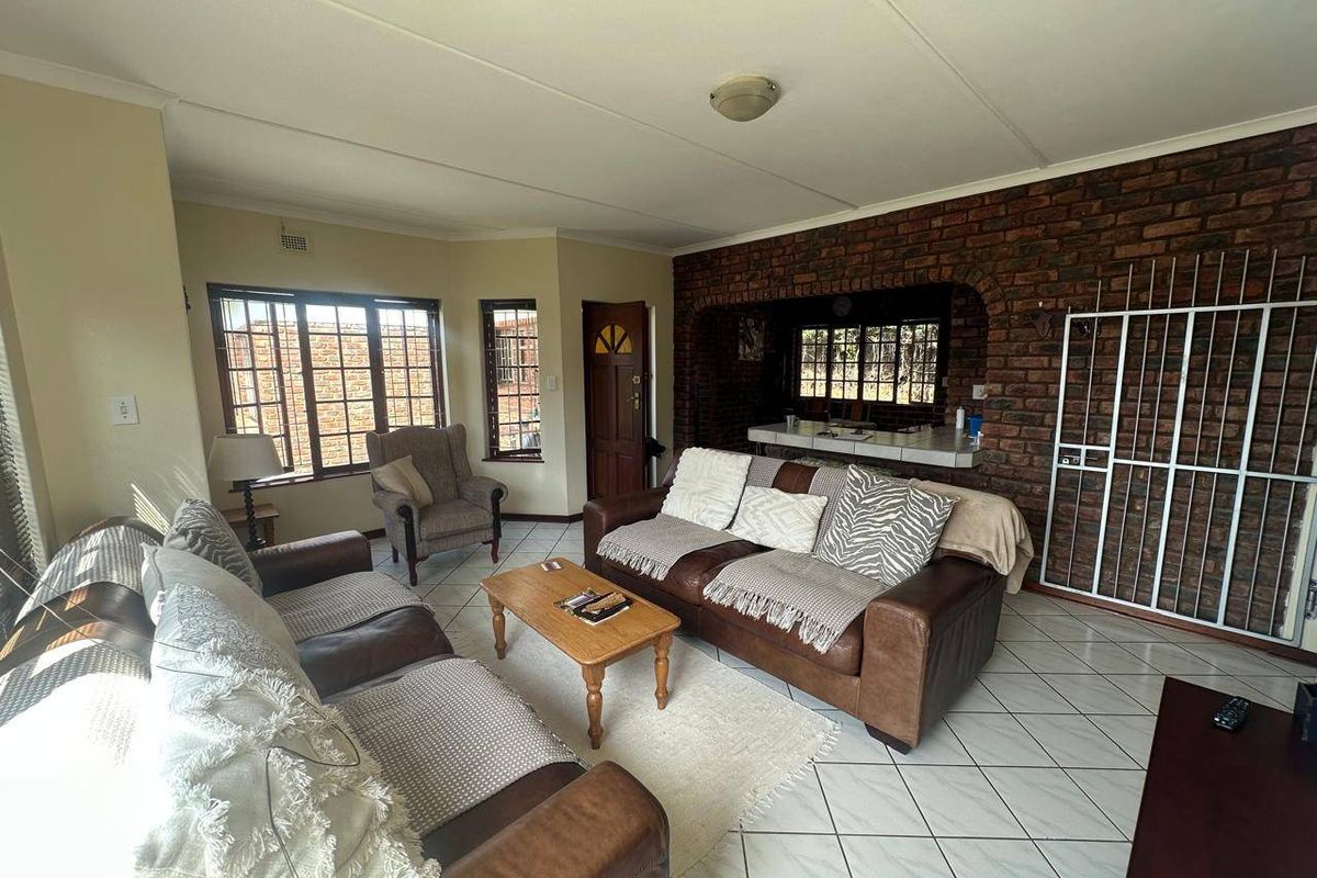 Spacious living room featuring an exposed brick feature wall, tiled flooring, and a breakfast bar opening into the adjacent kitchen area.