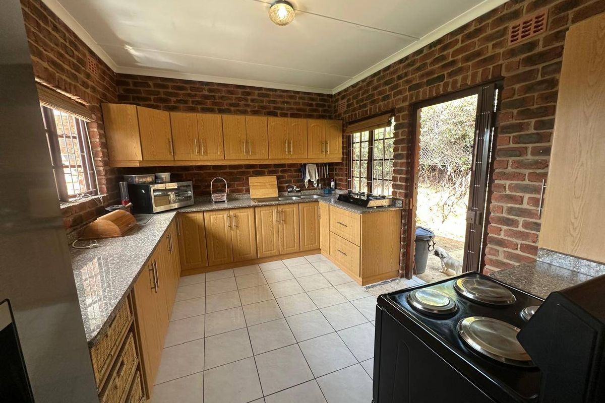 A functional kitchen featuring exposed brick walls, laminate cabinetry, granite countertops, and direct access to the rear exterior.
