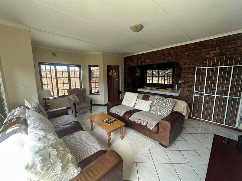 Spacious living room featuring an exposed brick feature wall, tiled flooring, and a breakfast bar opening into the adjacent kitchen area.