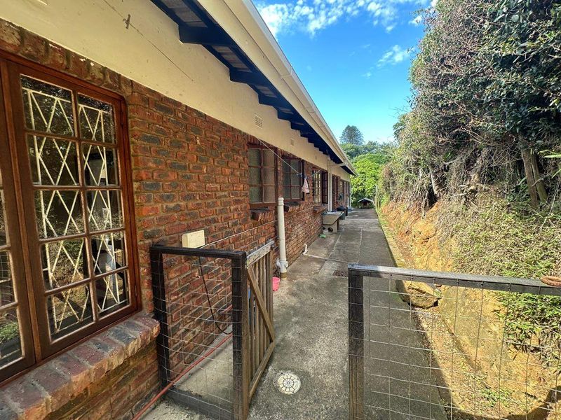 A side exterior view of the property featuring a brick facade, concrete pathway, and metal security gate along the side of the house.