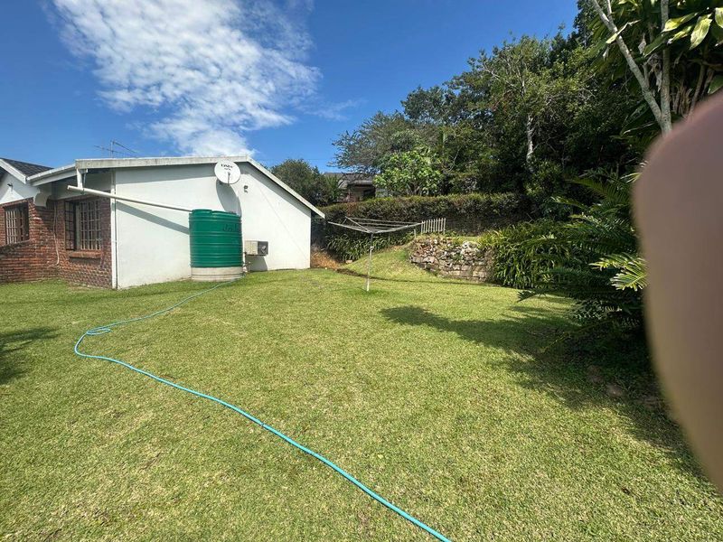 A rear garden area featuring a lawn, a water storage tank, a retaining wall, and a rotary clothesline.