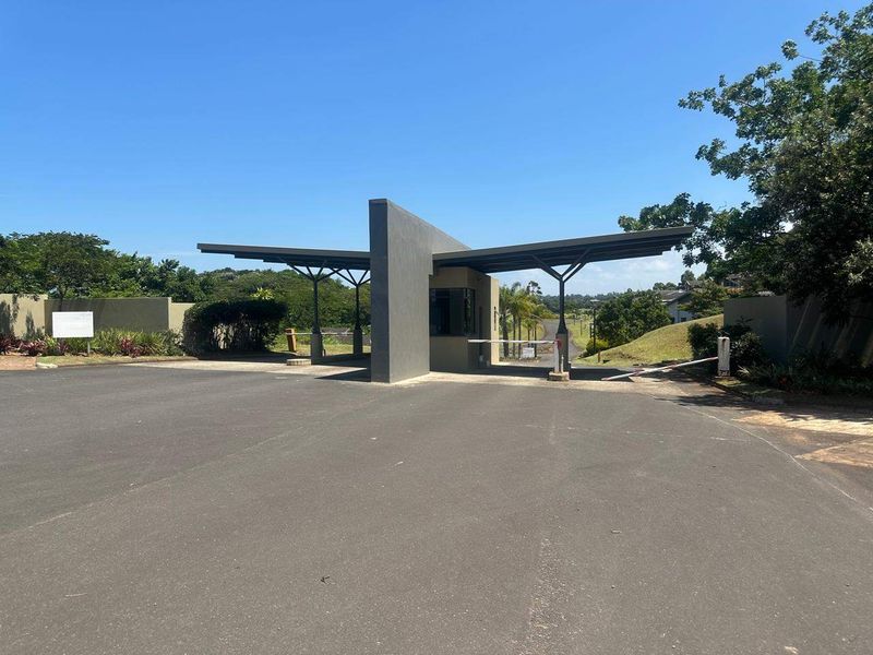 A modern security gatehouse entrance featuring a sleek architectural design, boom gate access, and paved driveway leading into the residential estate.
