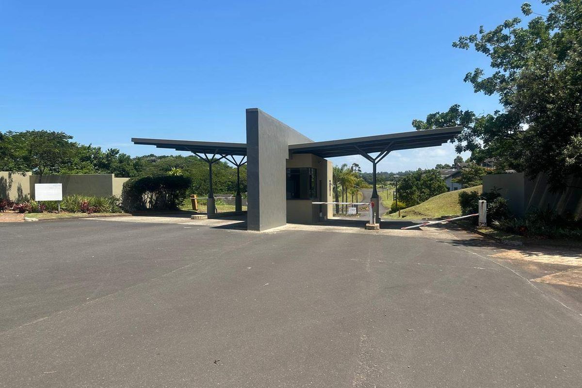 A modern security gatehouse entrance featuring a sleek architectural design, boom gate access, and paved driveway leading into the residential estate.