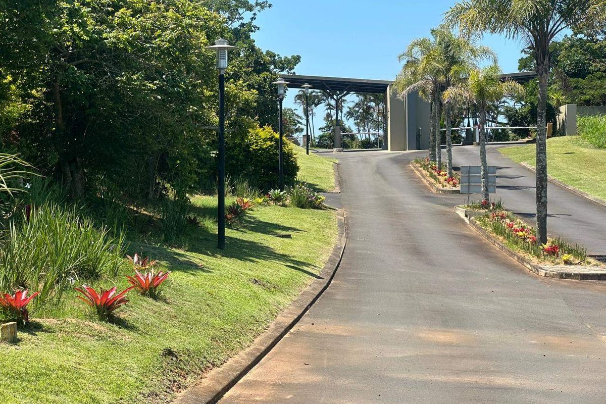 A well-maintained asphalt driveway leading to a secure gated entrance, surrounded by landscaped gardens and mature trees.