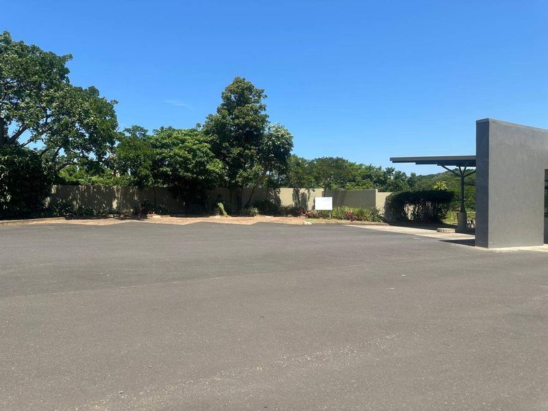 A spacious paved driveway area featuring a modern perimeter wall and a covered entrance structure, set within a well-maintained residential property.