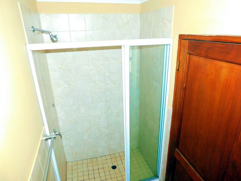 A functional shower stall featuring tiled walls, a floor drain, and a white-framed glass enclosure, situated adjacent to a wooden door.