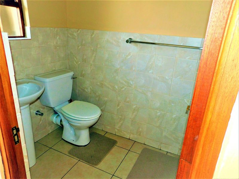 A functional bathroom featuring a pedestal basin, standard toilet, and tiled walls with a mounted towel rail.
