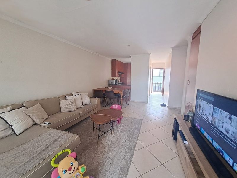 Open-plan living and dining area featuring tiled flooring, leading towards a kitchen and a balcony entrance.