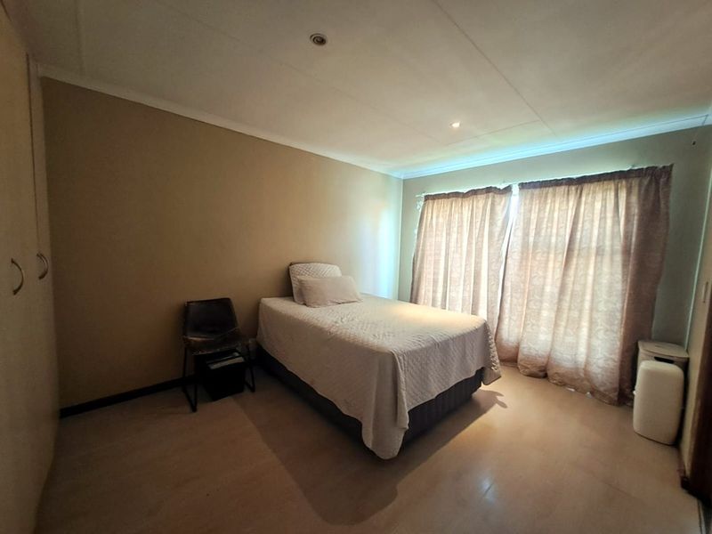 A functional bedroom featuring built-in cupboards, neutral wall tones, and large windows with curtains, providing a simple and comfortable living space.