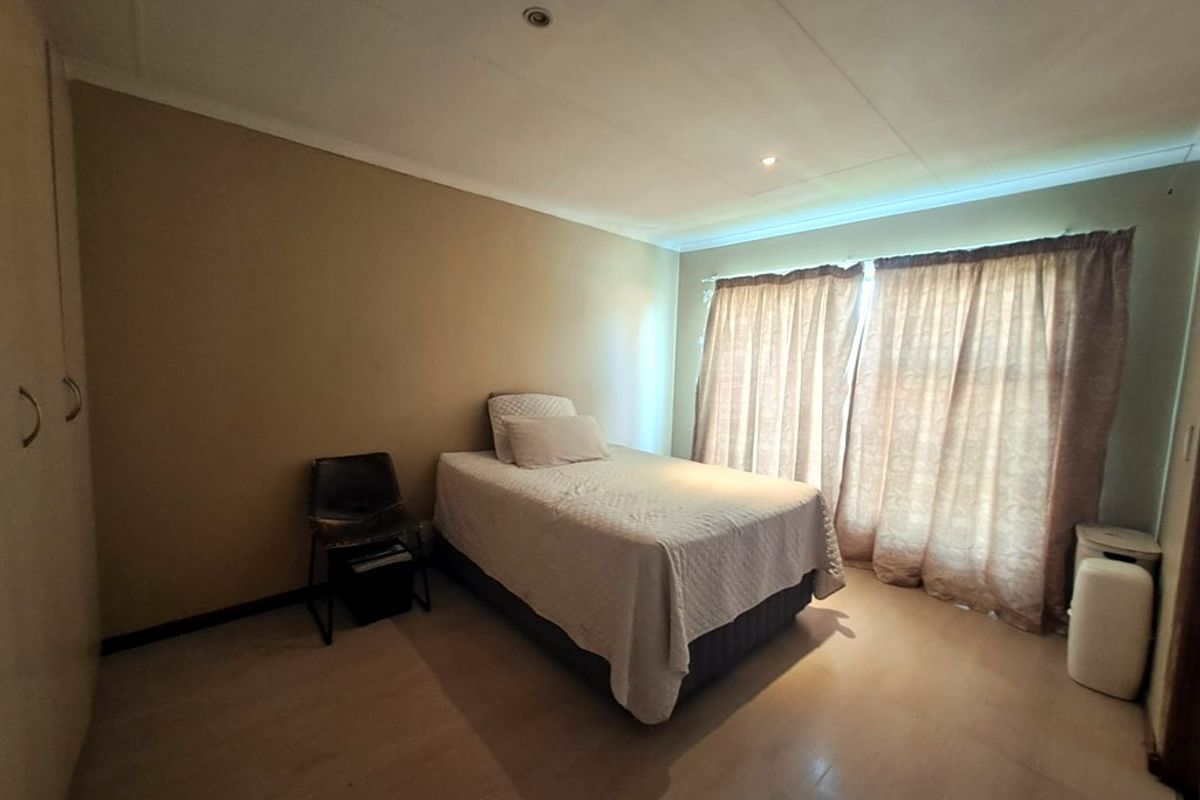 A functional bedroom featuring built-in cupboards, neutral wall tones, and large windows with curtains, providing a simple and comfortable living space.
