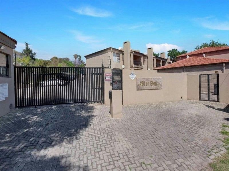 The entrance to the 420 on Eton apartment complex, featuring a paved driveway, secure metal gate, and perimeter walling.