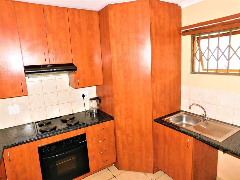 A functional kitchen featuring wood-finish cabinetry, granite countertops, a built-in oven with hob, extractor fan, and a stainless steel sink.