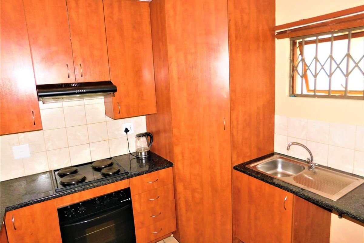 A functional kitchen featuring wood-finish cabinetry, granite countertops, a built-in oven with hob, extractor fan, and a stainless steel sink.