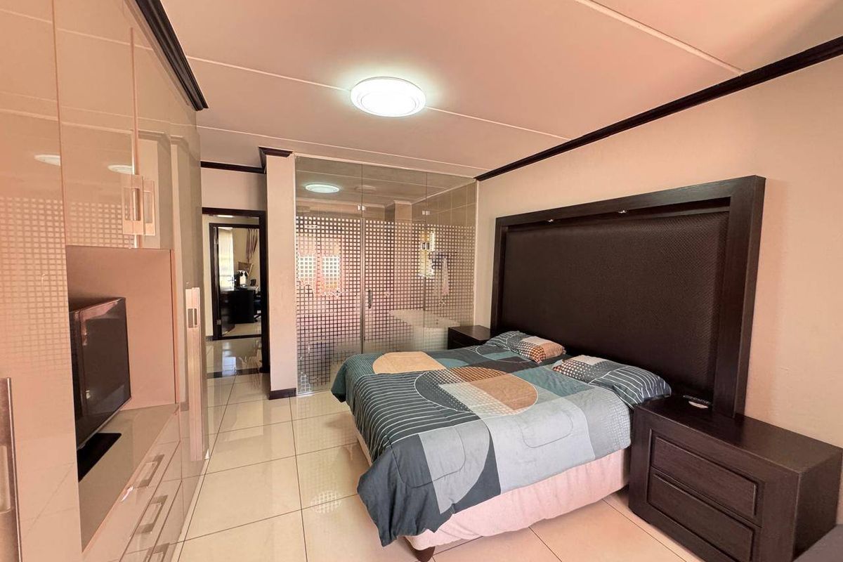 A modern bedroom featuring tiled flooring, extensive built-in cabinetry, and a glass-partitioned en-suite bathroom, creating an open and contemporary living space.