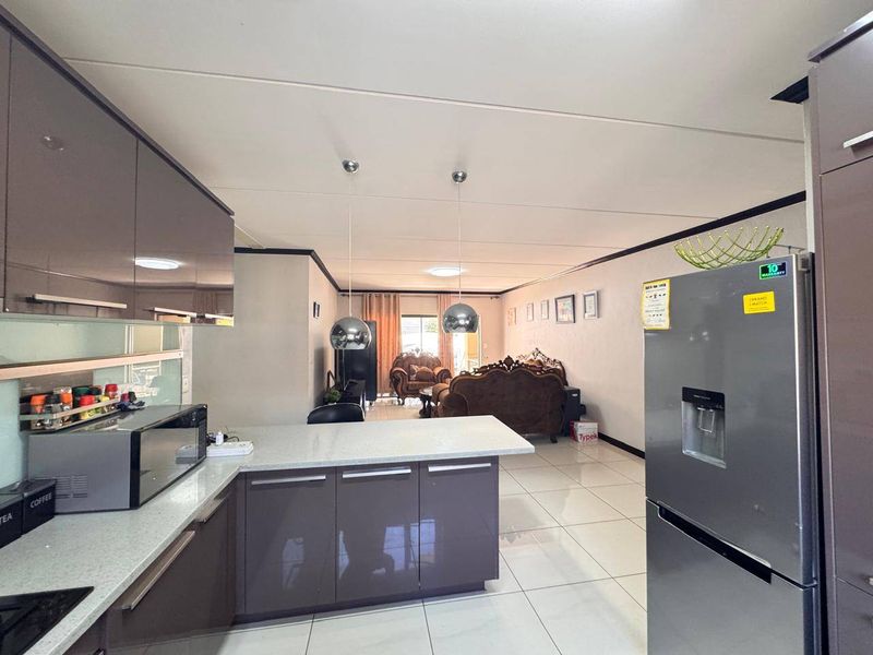 Modern open-plan kitchen and living area featuring glossy cabinetry, stone countertops, pendant lighting, and neutral tiled flooring throughout.