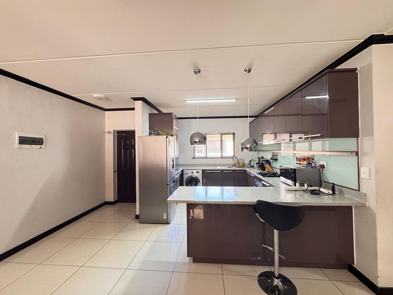 Modern kitchen featuring high-gloss cabinetry, stone countertops, a breakfast bar, and integrated appliances, complemented by neutral tiled flooring and contemporary pendant lighting.