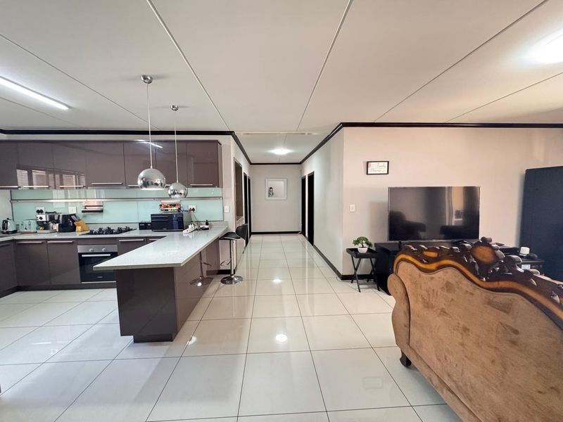 Modern open-plan living area featuring a sleek kitchen with glossy cabinetry, stone countertops, and high-gloss floor tiles throughout the spacious layout.