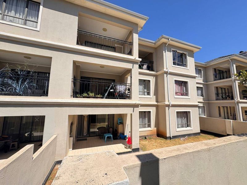 Rear view of a multi-story apartment complex featuring private balconies with wrought iron railings and ground-floor patio access.
