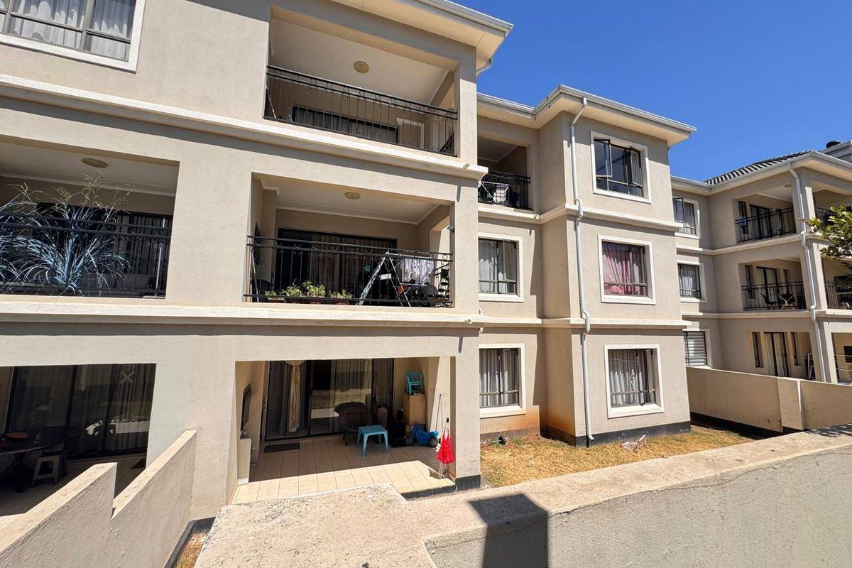 Rear view of a multi-story apartment complex featuring private balconies with wrought iron railings and ground-floor patio access.