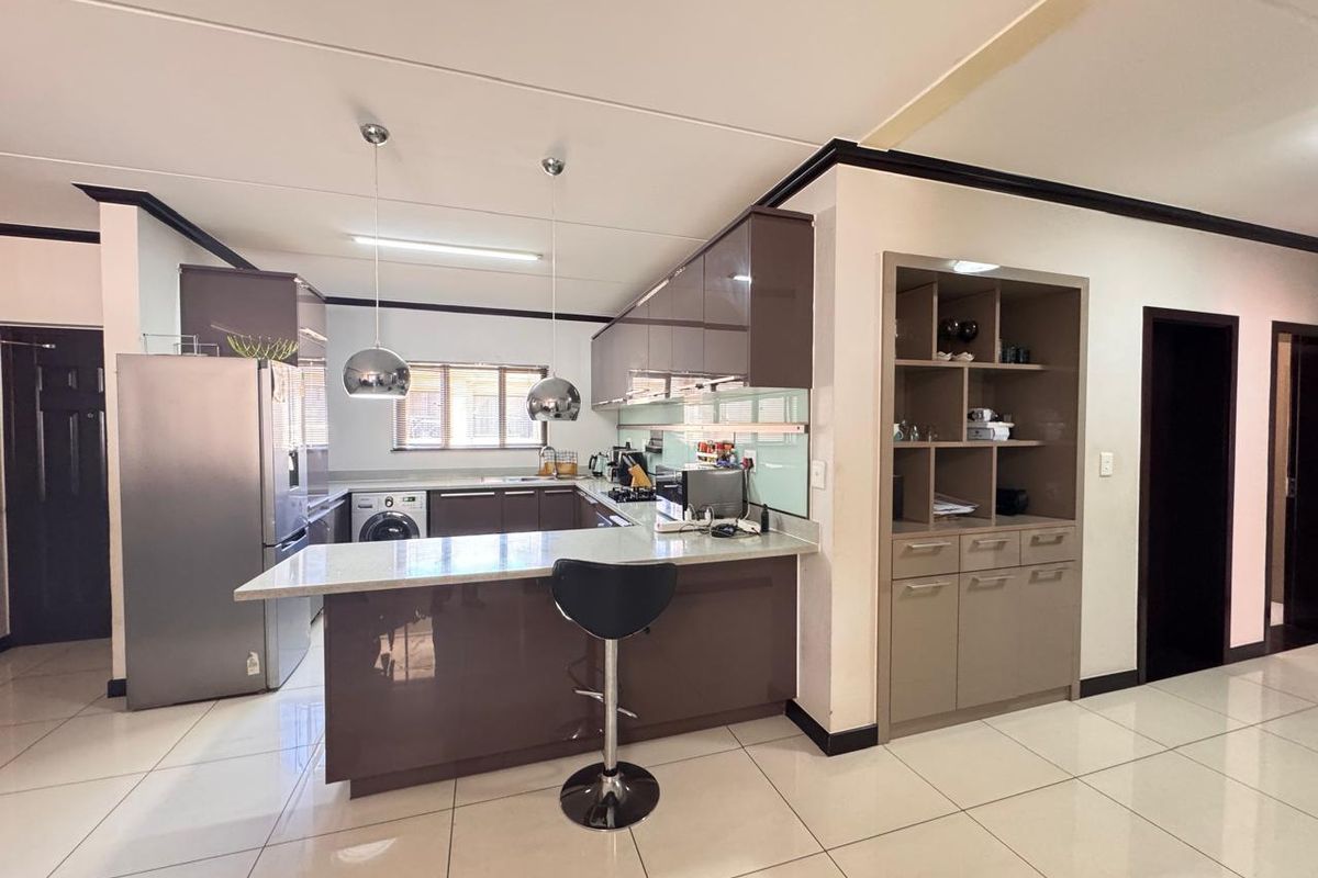 Modern kitchen featuring high-gloss cabinetry, stone countertops, a breakfast bar, and integrated shelving, complemented by sleek tiled flooring and contemporary pendant lighting.