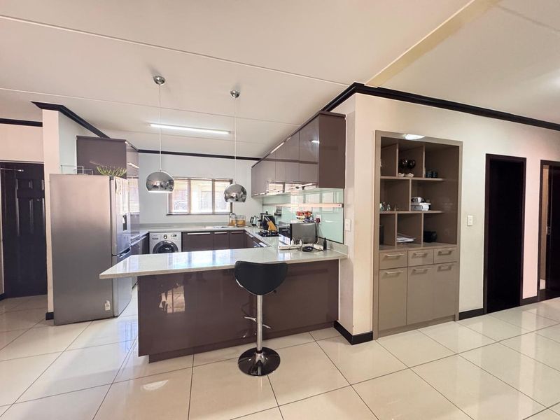 Modern kitchen featuring high-gloss cabinetry, stone countertops, a breakfast bar, and integrated shelving, complemented by sleek tiled flooring and contemporary pendant lighting.