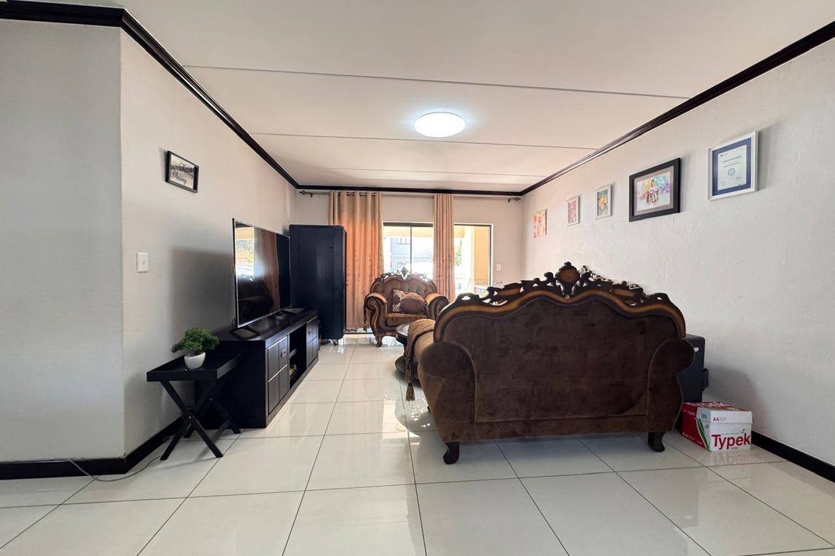 Spacious living room featuring large format floor tiles, dark crown molding, and a sliding glass door providing access to the outdoor area.