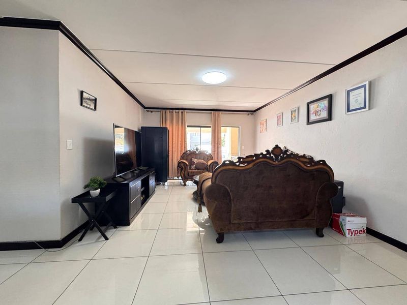 Spacious living room featuring large format floor tiles, dark crown molding, and a sliding glass door providing access to the outdoor area.