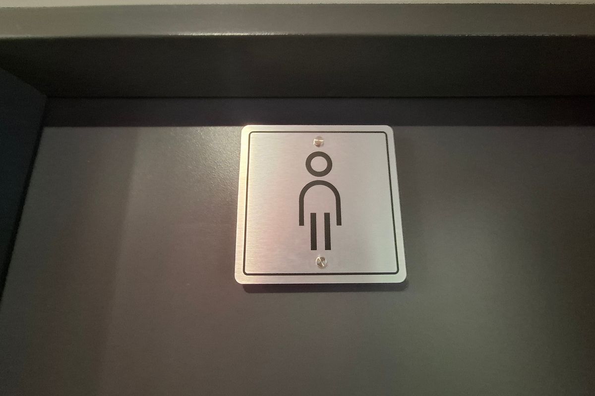 A close-up view of a modern, brushed metal male restroom signage mounted on a dark grey door.