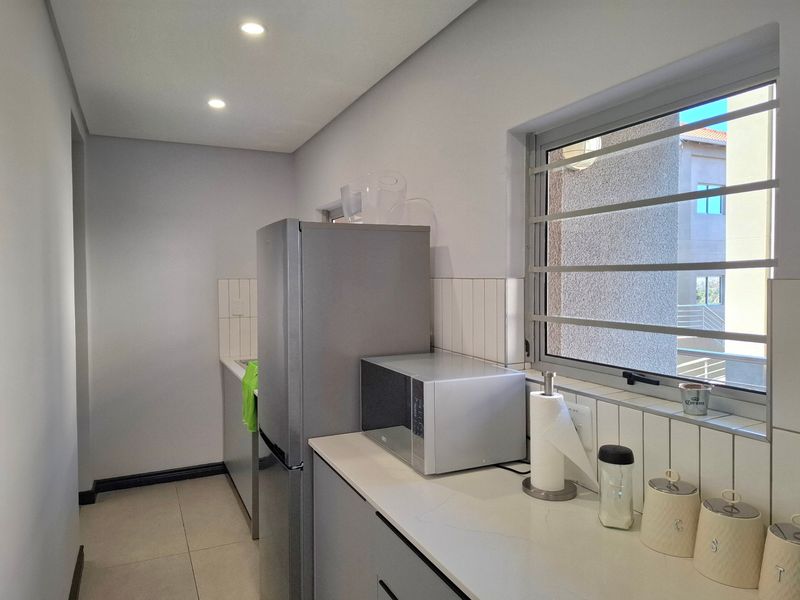 A clean, modern kitchen featuring neutral cabinetry, stone countertops, a tiled backsplash, and recessed lighting, providing a functional and well-maintained workspace.