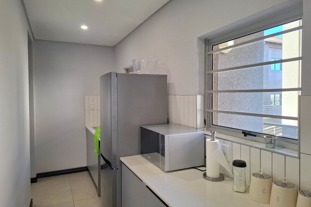A clean, modern kitchen featuring neutral cabinetry, stone countertops, a tiled backsplash, and recessed lighting, providing a functional and well-maintained workspace.