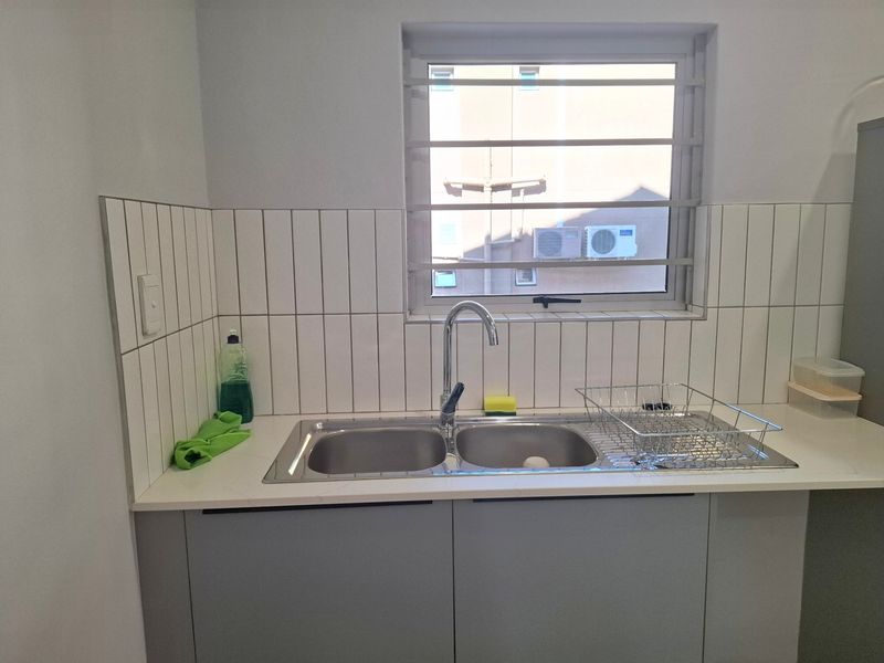 A clean and functional scullery area featuring a double bowl stainless steel sink, modern chrome tap, and contemporary vertical subway tile backsplash.