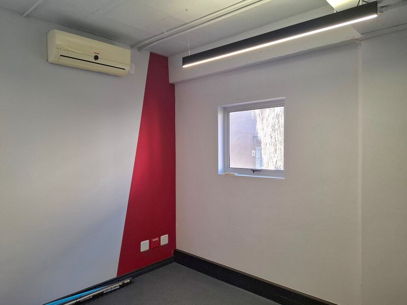 A clean, empty office space featuring a split-system air conditioner, modern linear lighting, and a distinct red accent wall.