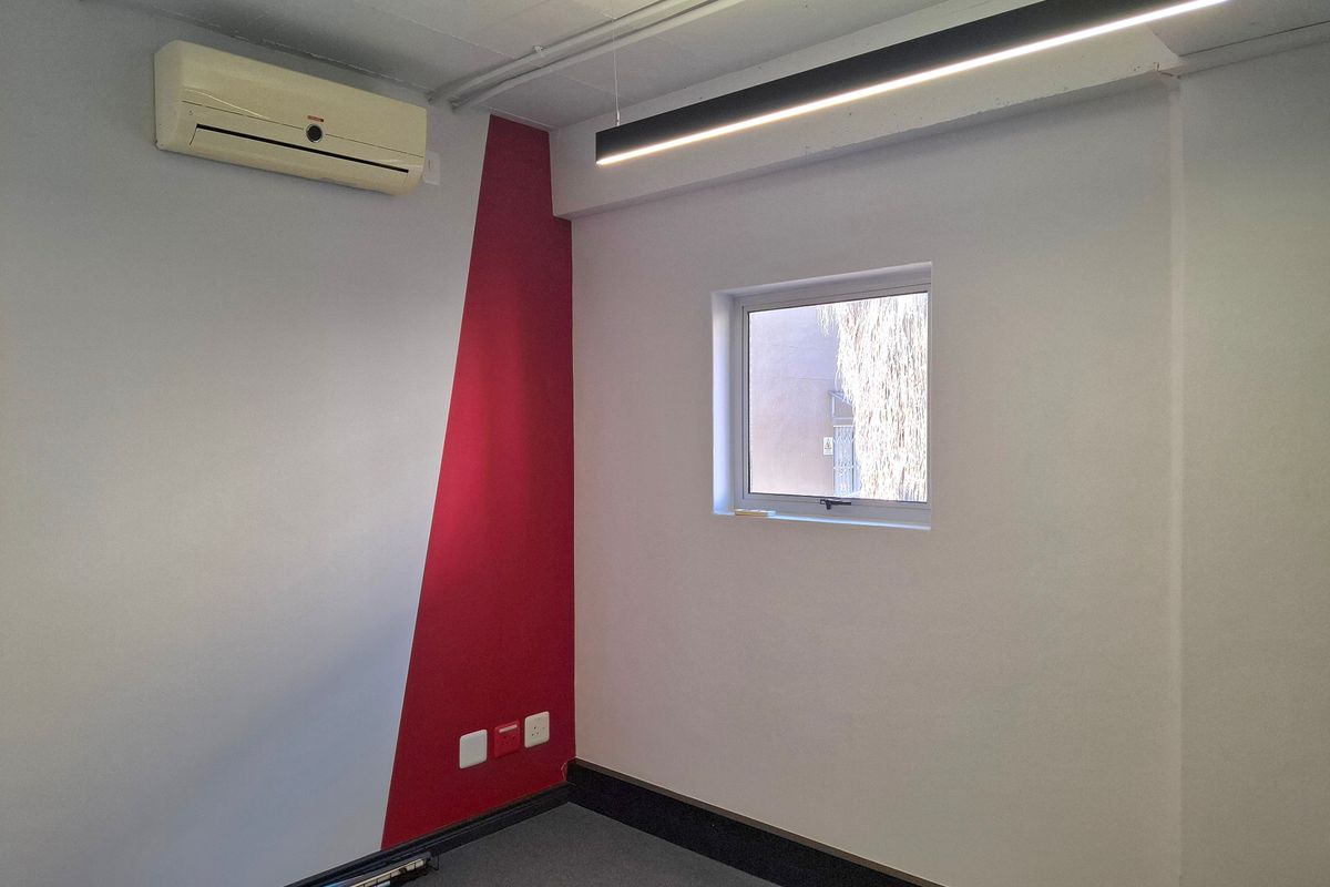 A clean, empty office space featuring a split-system air conditioner, modern linear lighting, and a distinct red accent wall.