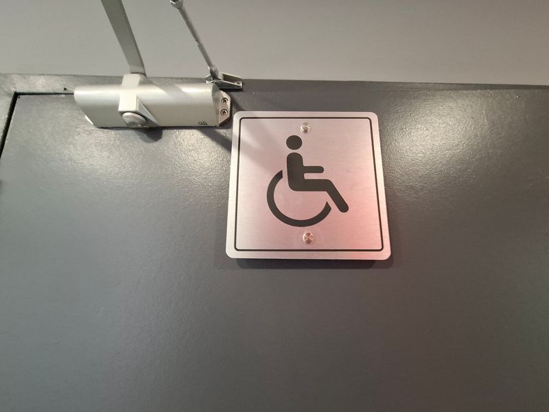 A close-up view of a commercial door featuring an accessibility sign and a hydraulic door closer mechanism.