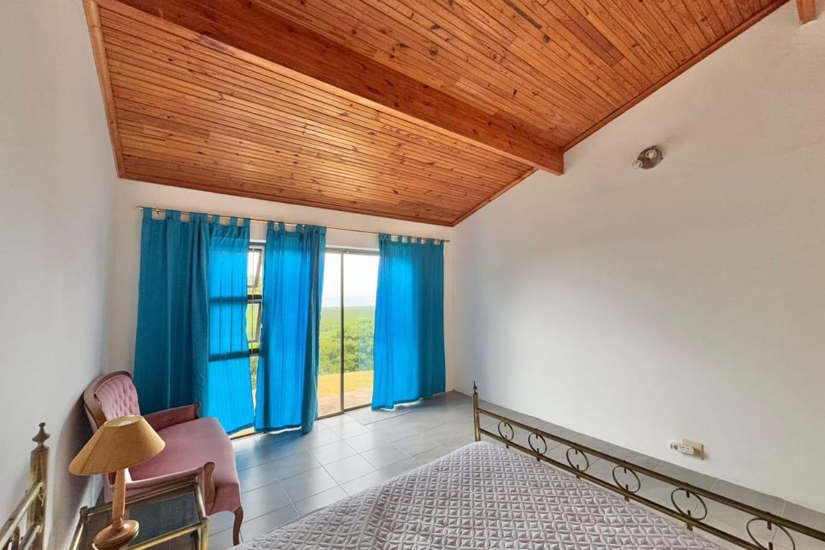 A bedroom featuring a vaulted timber-clad ceiling, tiled flooring, and sliding glass doors that open to a scenic outdoor view.