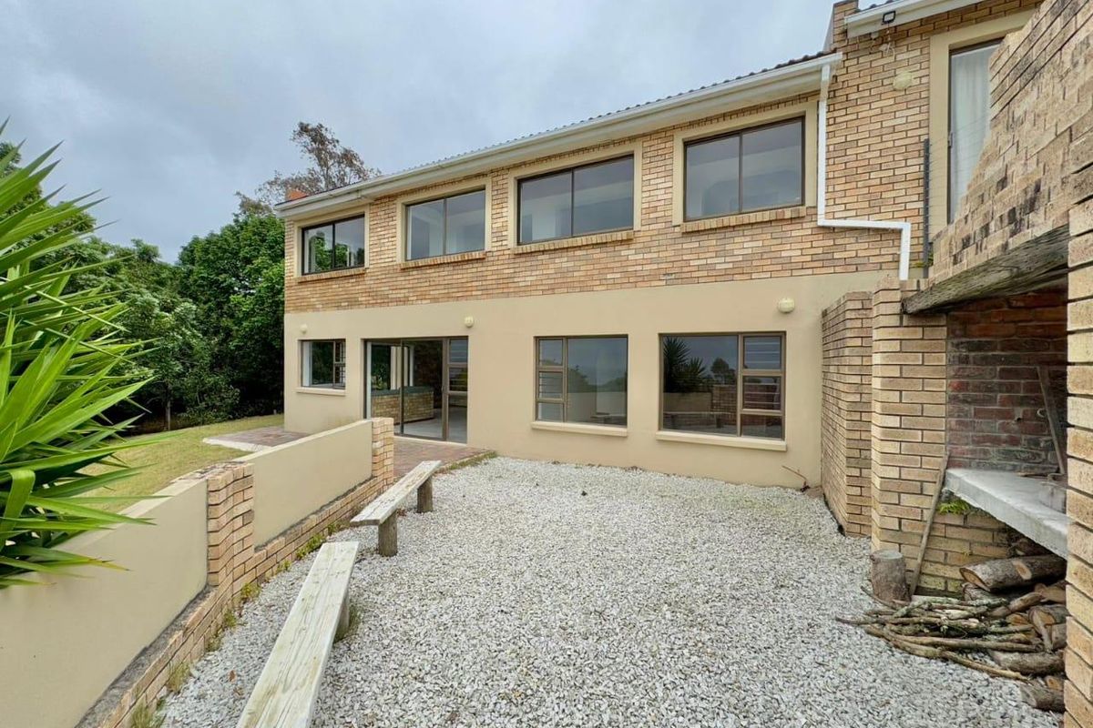 Rear exterior view of a brick farmhouse featuring a gravel courtyard, built-in braai area, and large sliding windows overlooking the garden.
