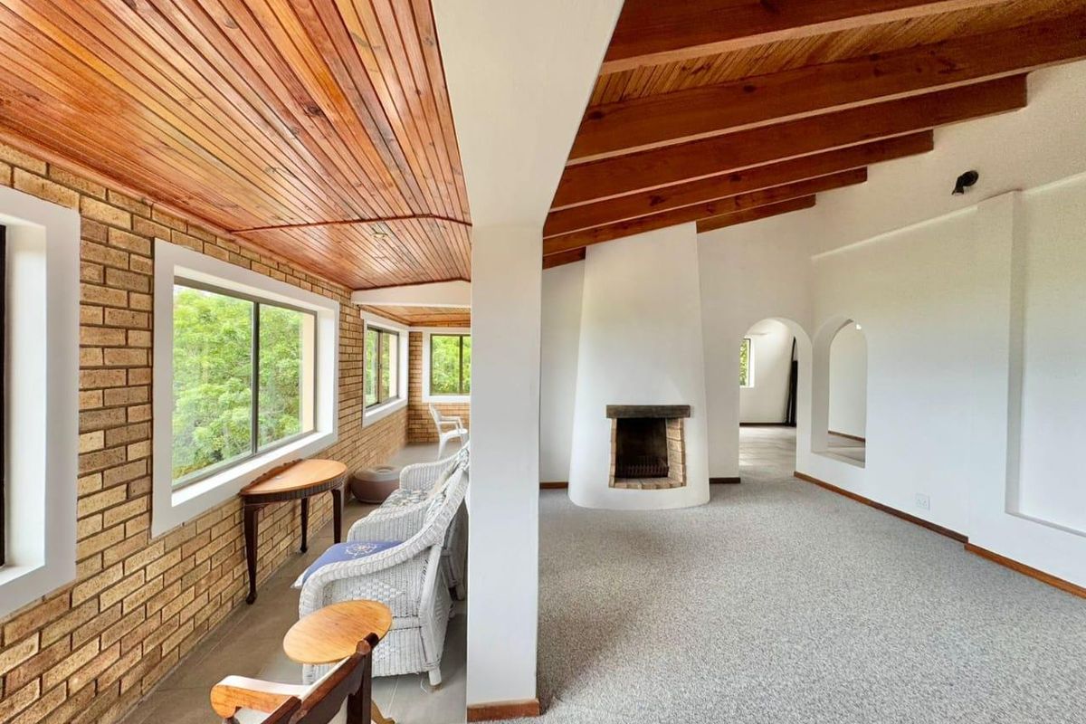 Spacious living area featuring a unique built-in fireplace, exposed timber ceiling, and a charming brick feature wall with large windows overlooking the garden.