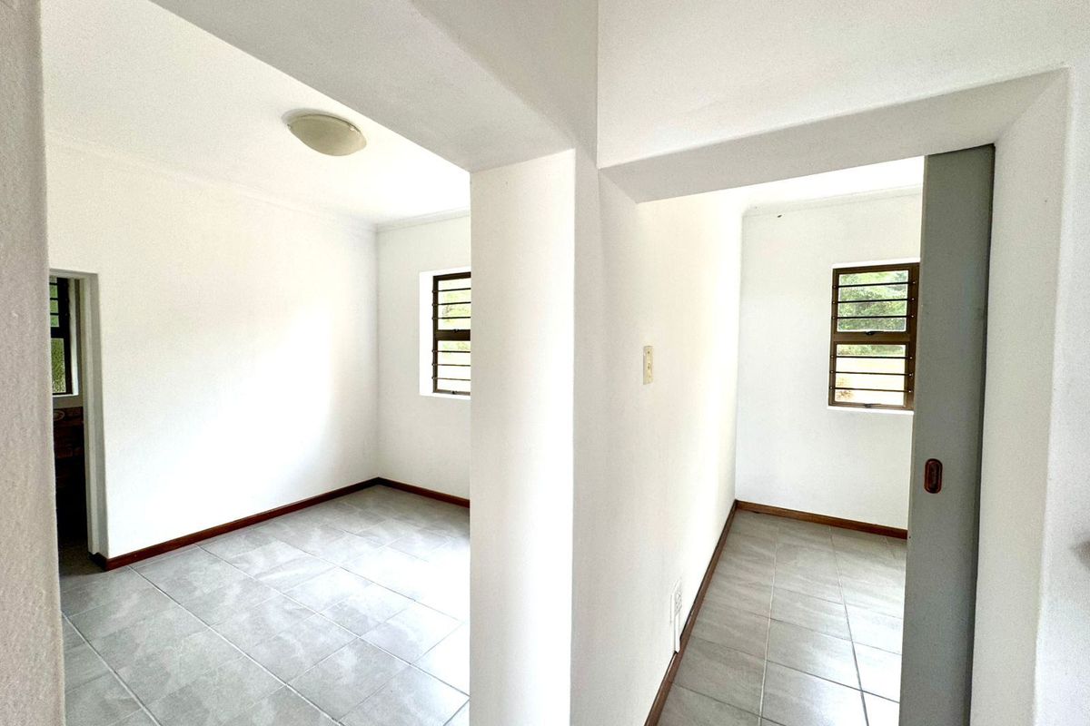 An empty, neutral-toned bedroom featuring tiled flooring, large windows with security bars, and clean white walls, offering a blank canvas for personalization.