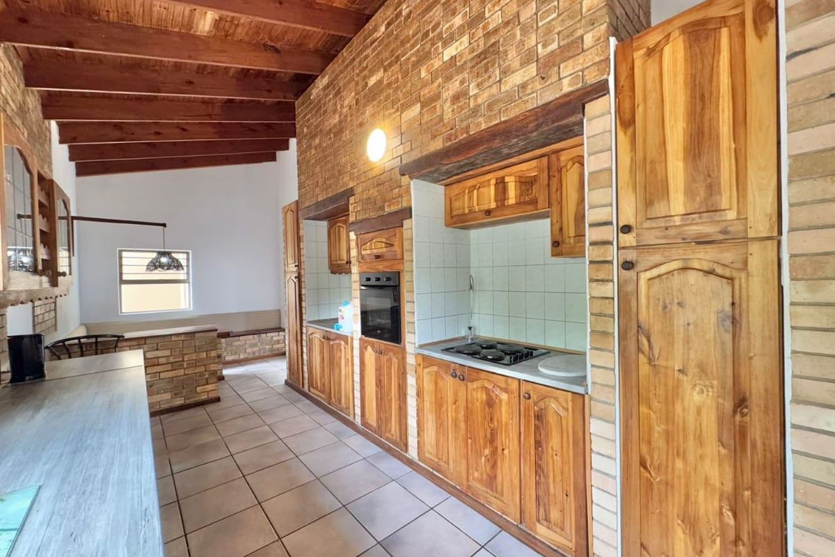 Rustic kitchen featuring exposed timber beams, brick feature walls, and extensive built-in wooden cabinetry with integrated oven and hob.