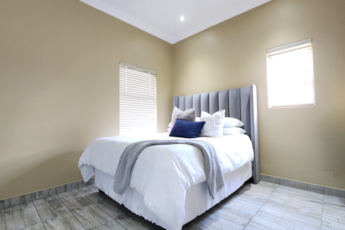 A well-maintained bedroom featuring neutral wall tones, tiled flooring, and dual windows fitted with venetian blinds.