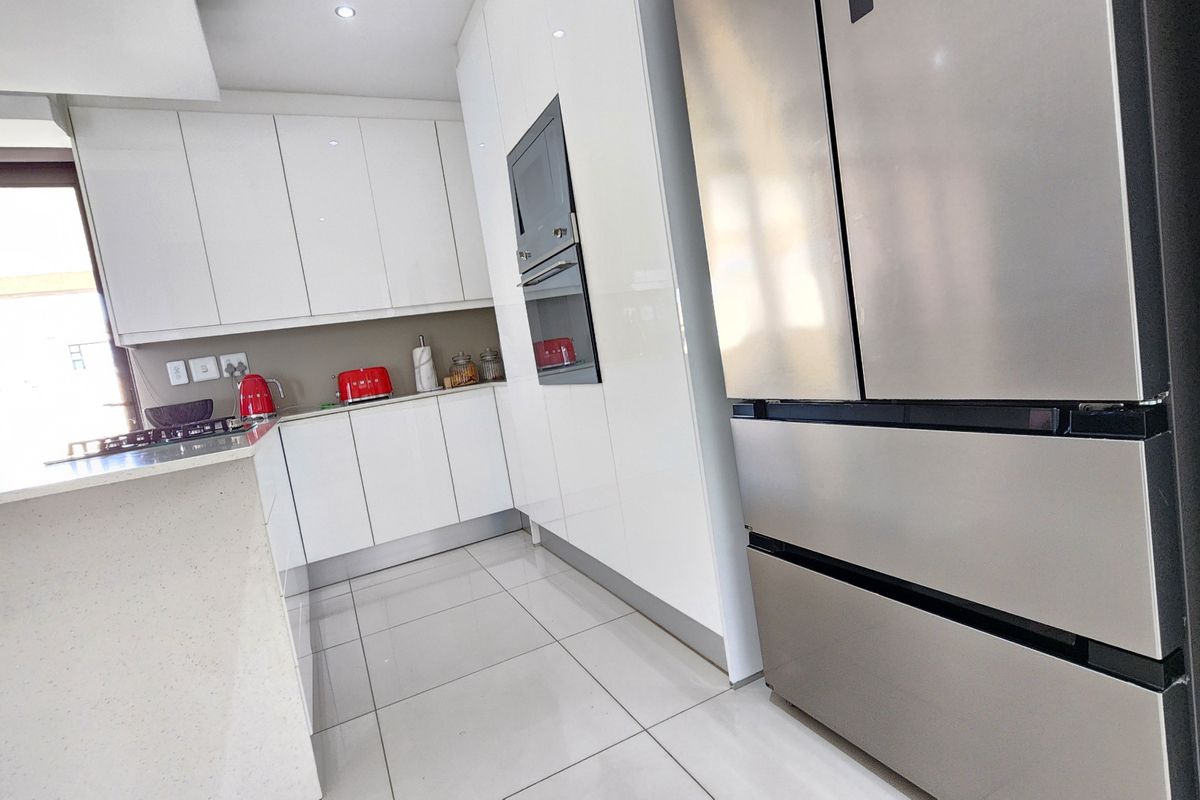 Modern kitchen featuring sleek white gloss cabinetry, stone countertops, integrated appliances, and polished floor tiles in a bright, contemporary layout.
