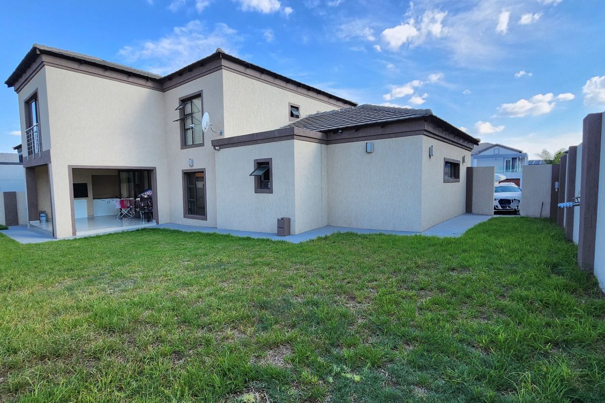 Rear view of a modern double-story house featuring a spacious lawn, covered patio area, and secure boundary walling.