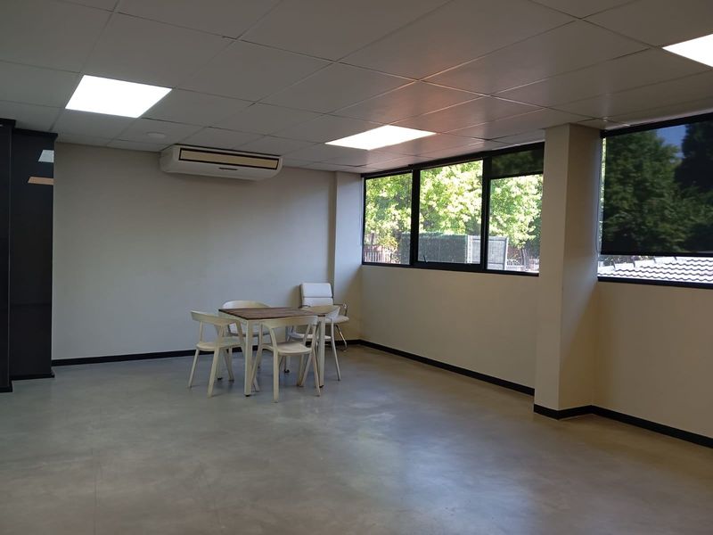 A spacious commercial office area featuring a suspended ceiling, recessed lighting, polished concrete flooring, and a wall-mounted air conditioning unit.