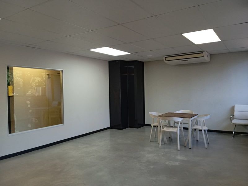 A functional commercial office space featuring a polished concrete floor, suspended ceiling with recessed lighting, and a wall-mounted air conditioning unit.