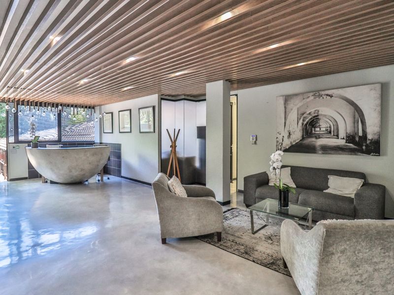 Modern commercial reception area featuring a unique curved concrete reception desk, polished concrete flooring, and a distinctive slatted timber ceiling with integrated lighting.