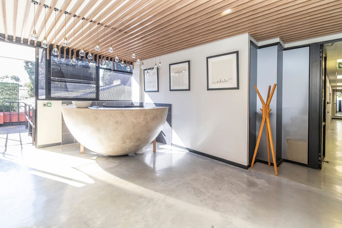 Modern commercial reception area featuring polished concrete floors, a unique curved built-in desk, and a stylish slatted timber ceiling with pendant lighting.