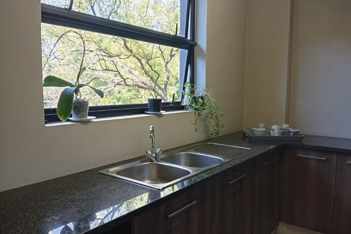A functional kitchen area featuring dark wood cabinetry, granite countertops, and a double stainless steel sink positioned beneath a large window.